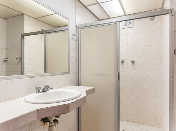 Un baño con lavamanos blanco, un espejo y cabina de ducha con paredes de vidrio.