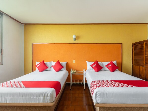 Habitación de hotel con dos camas, cada una con ropa de cama roja y blanca, cabeceros de madera y una pequeña mesa entre ellas.