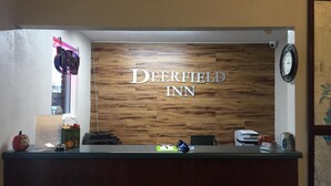 Un comptoir d’accueil avec un panneau en bois servant de décor, sur lequel on peut lire « Deerfield Inn » en lettres métalliques.