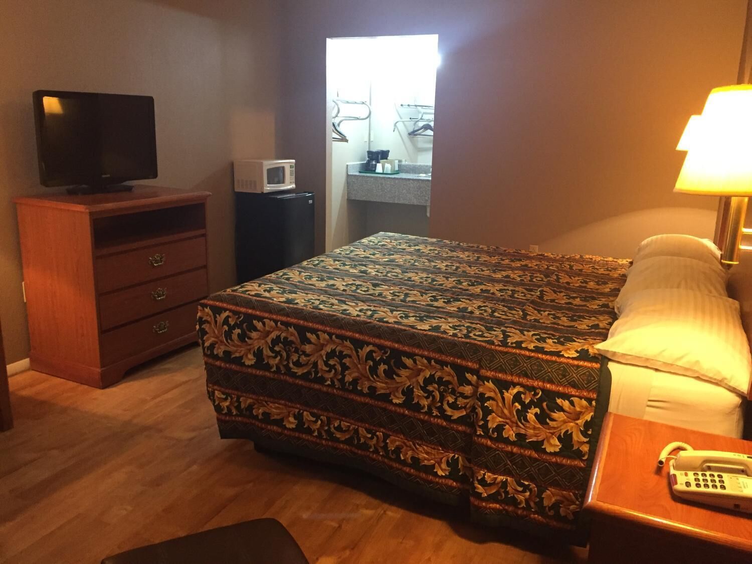Ein Hotelzimmer mit einem Bett, einem Schminktisch, einem Fernseher, einer Mikrowelle und einem Nachttisch mit Lampe und Telefon.