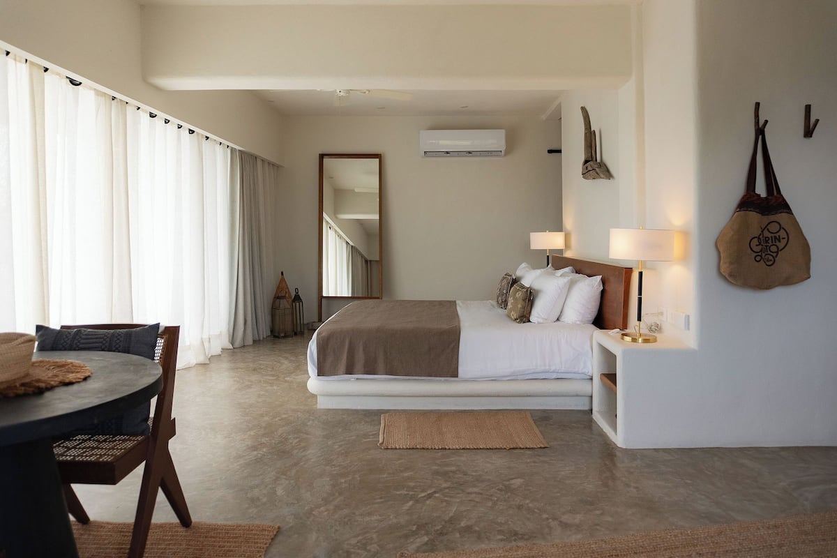 A modern hotel room with a large bed, a bedside table with lamps, a hanging bag, and a view of the hallway.