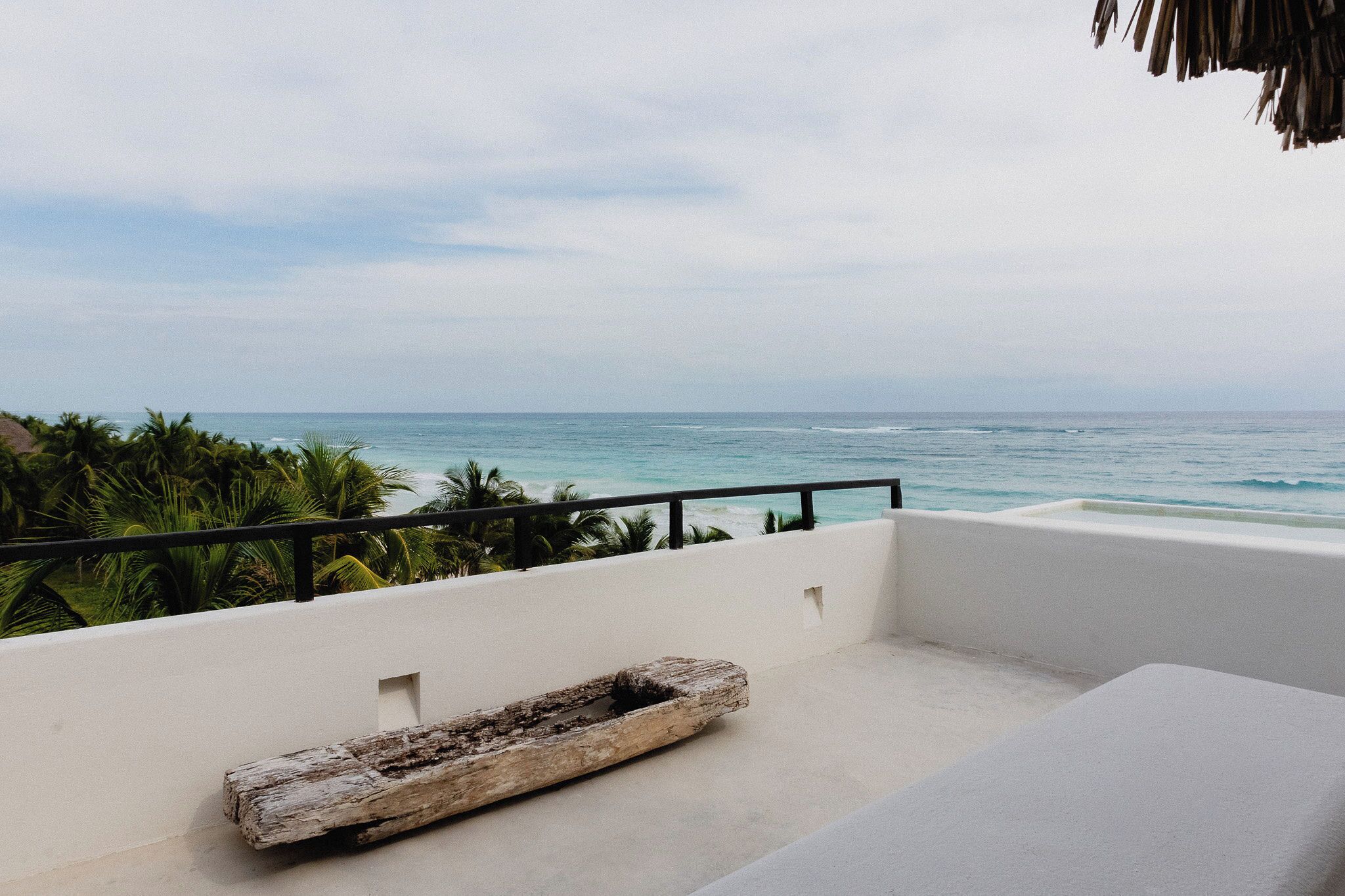 A balcony with a view of the ocean, a white wall, and a wooden bench.