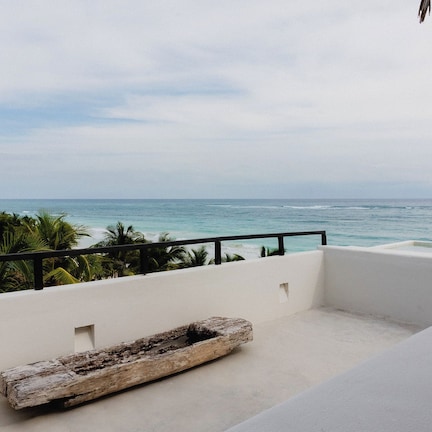 A balcony with a view of the ocean, a white wall, and a wooden bench.