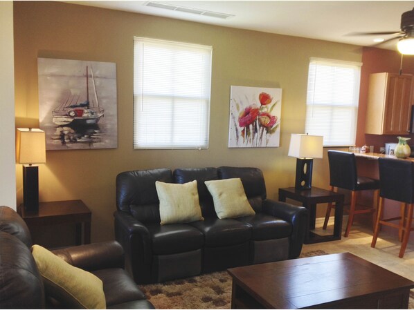 A living room with a black leather sofa, two lamps, a coffee table, and artwork on the walls. - Pacifico Resort Condominiums (Sardinal)