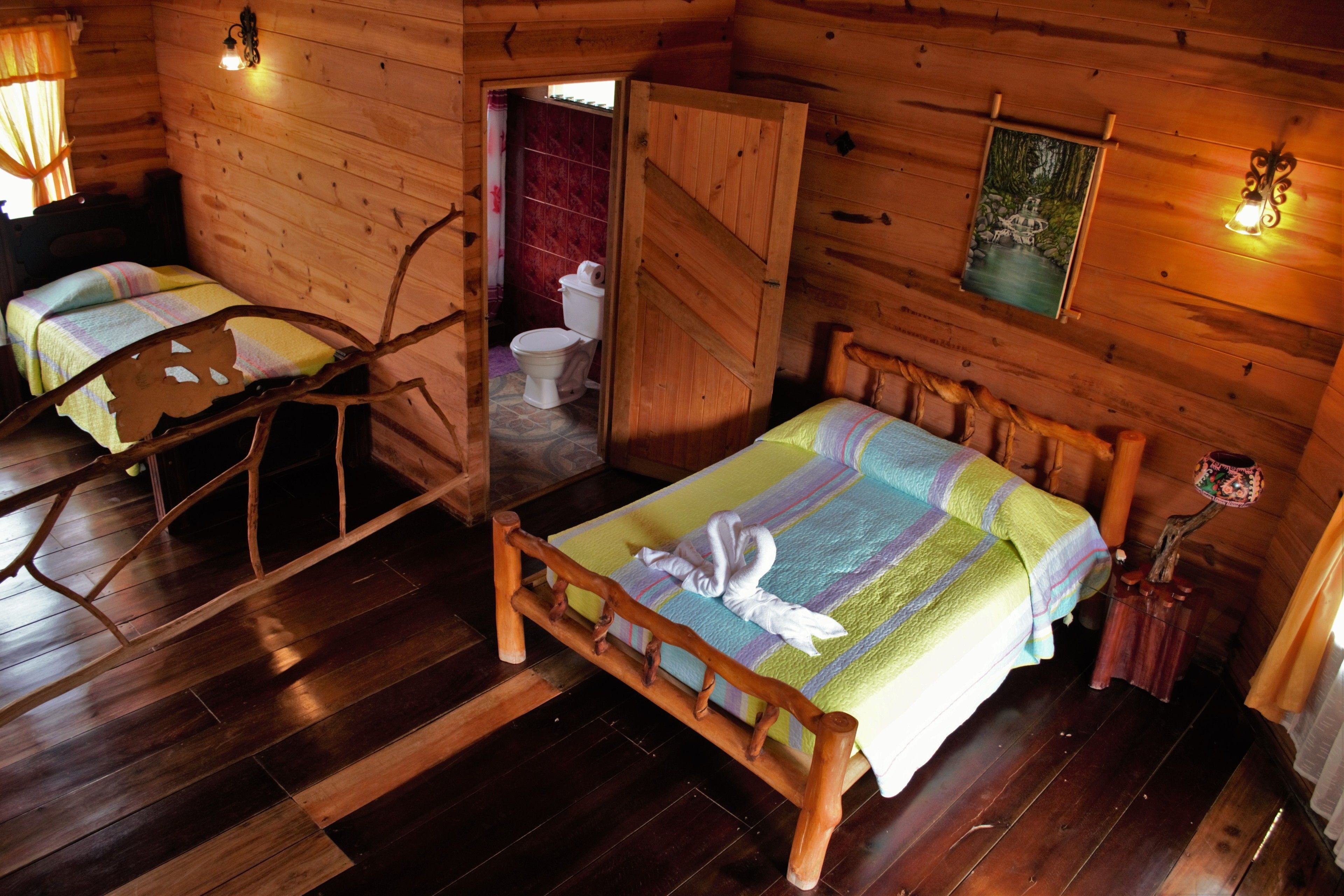 A wooden cabin with two beds, a wooden chair, a toilet, and a painting on the wall.
