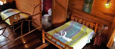 A wooden cabin with two beds, a wooden chair, a toilet, and a painting on the wall.