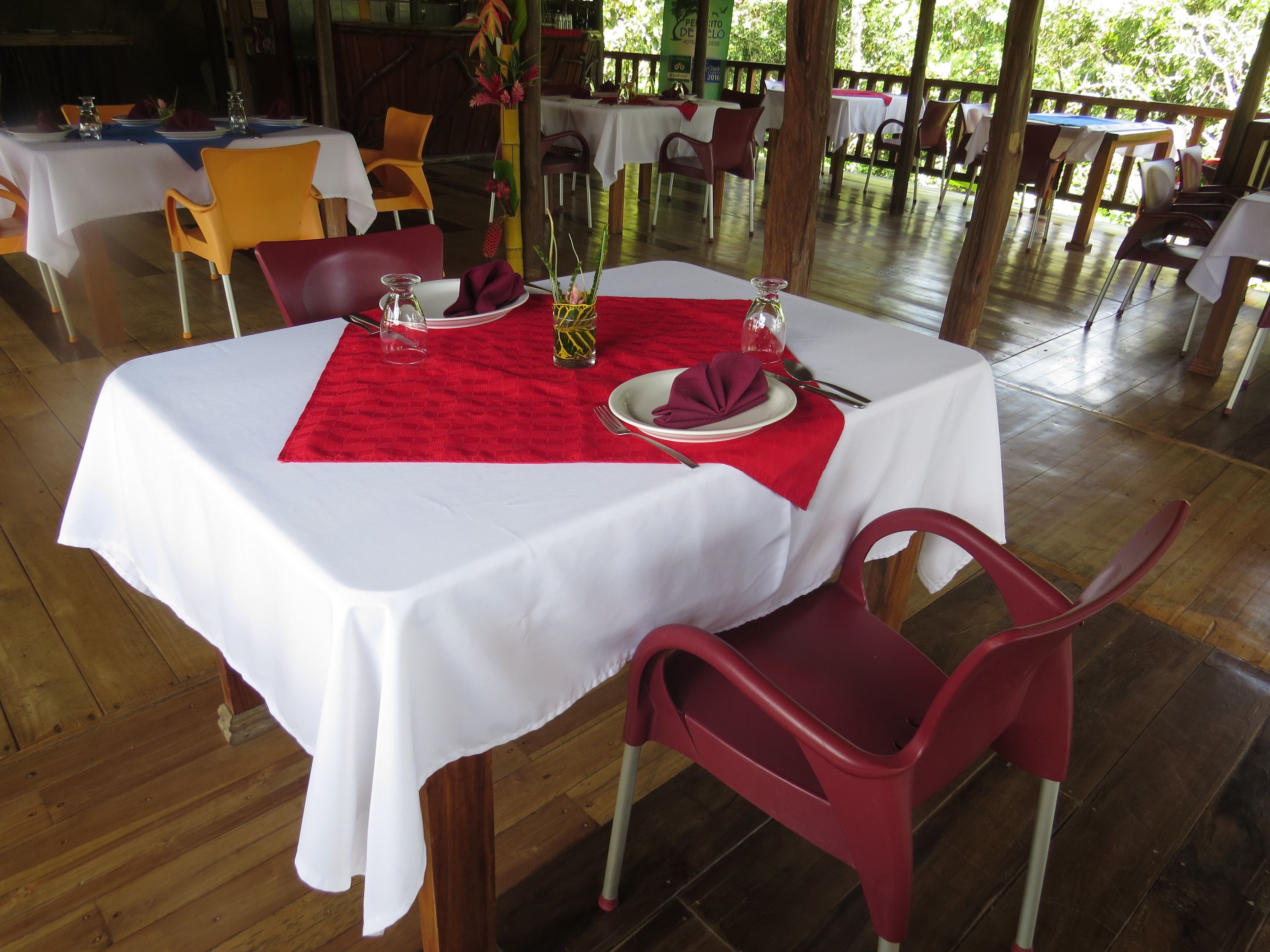 A dining area with tables set for two, featuring white tablecloths and red placemats.