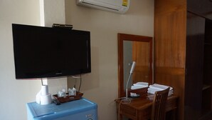 A room with a flat-screen TV mounted on the wall, a small blue refrigerator, a wooden desk with a chair, and a mirror on the wall.