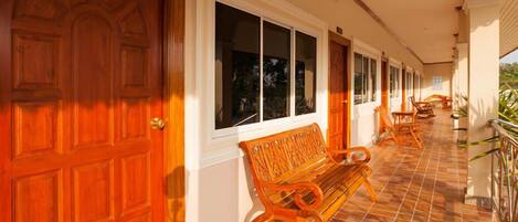 A covered corridor with wooden doors and windows, a bench, and outdoor furniture.