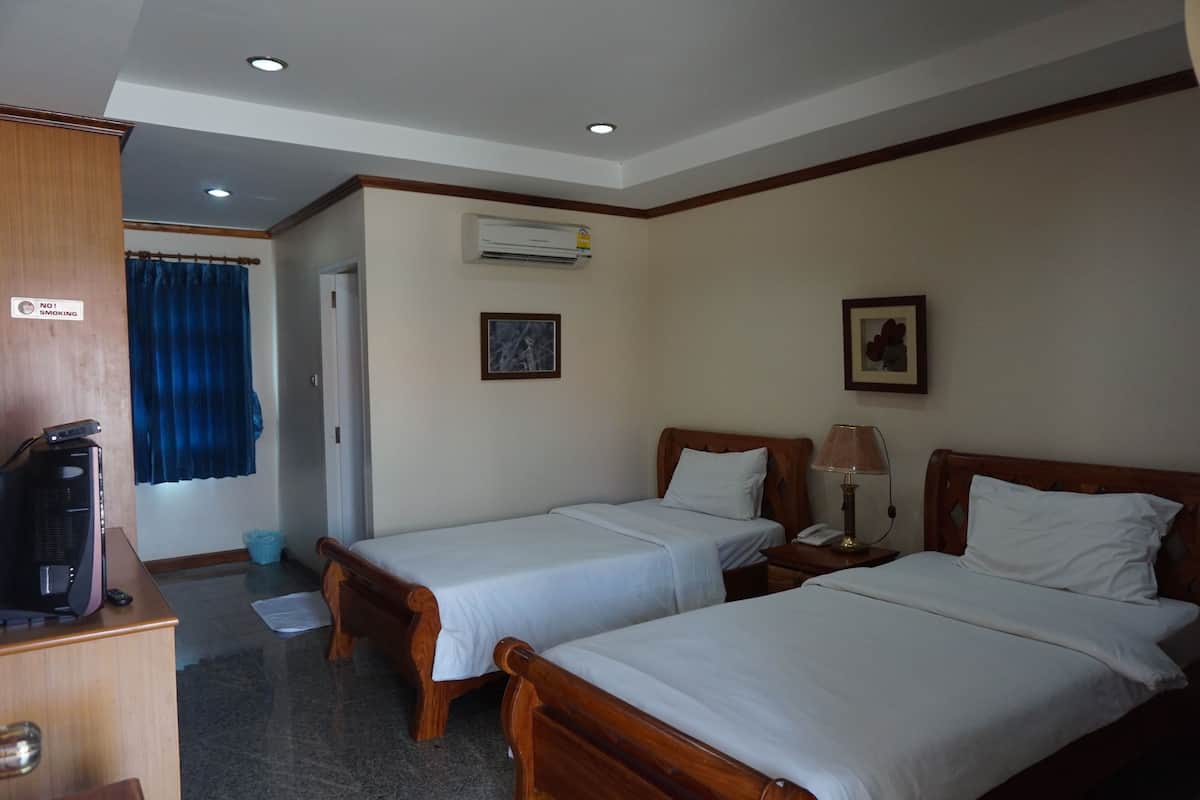 Habitación de hotel con dos camas individuales, un escritorio con computadora, un equipo de aire acondicionado y una cortina azul.