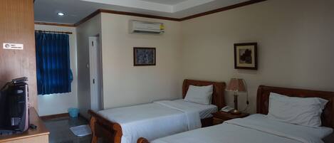 Une chambre d’hôtel avec deux lits simples, un bureau avec un ordinateur, un appareil de climatisation et un rideau bleu.