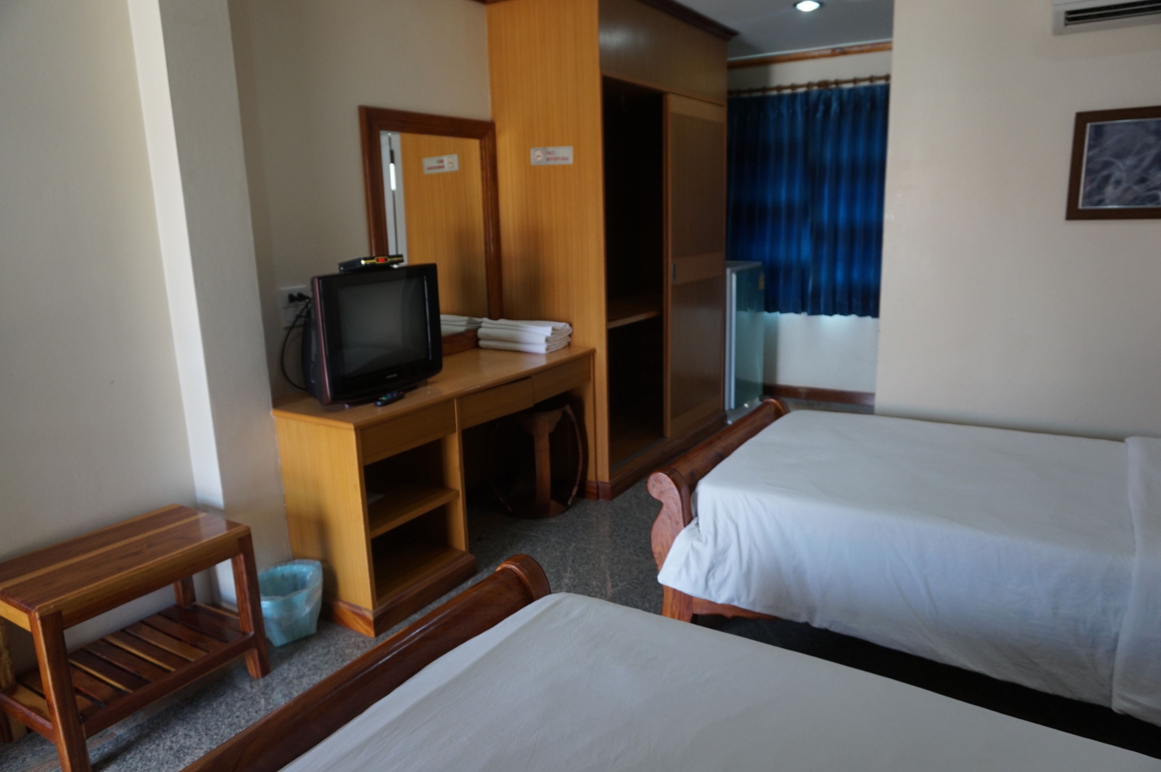 Habitación de hotel con dos camas, un televisor sobre un escritorio de madera, un taburete pequeño y un cubo de basura.