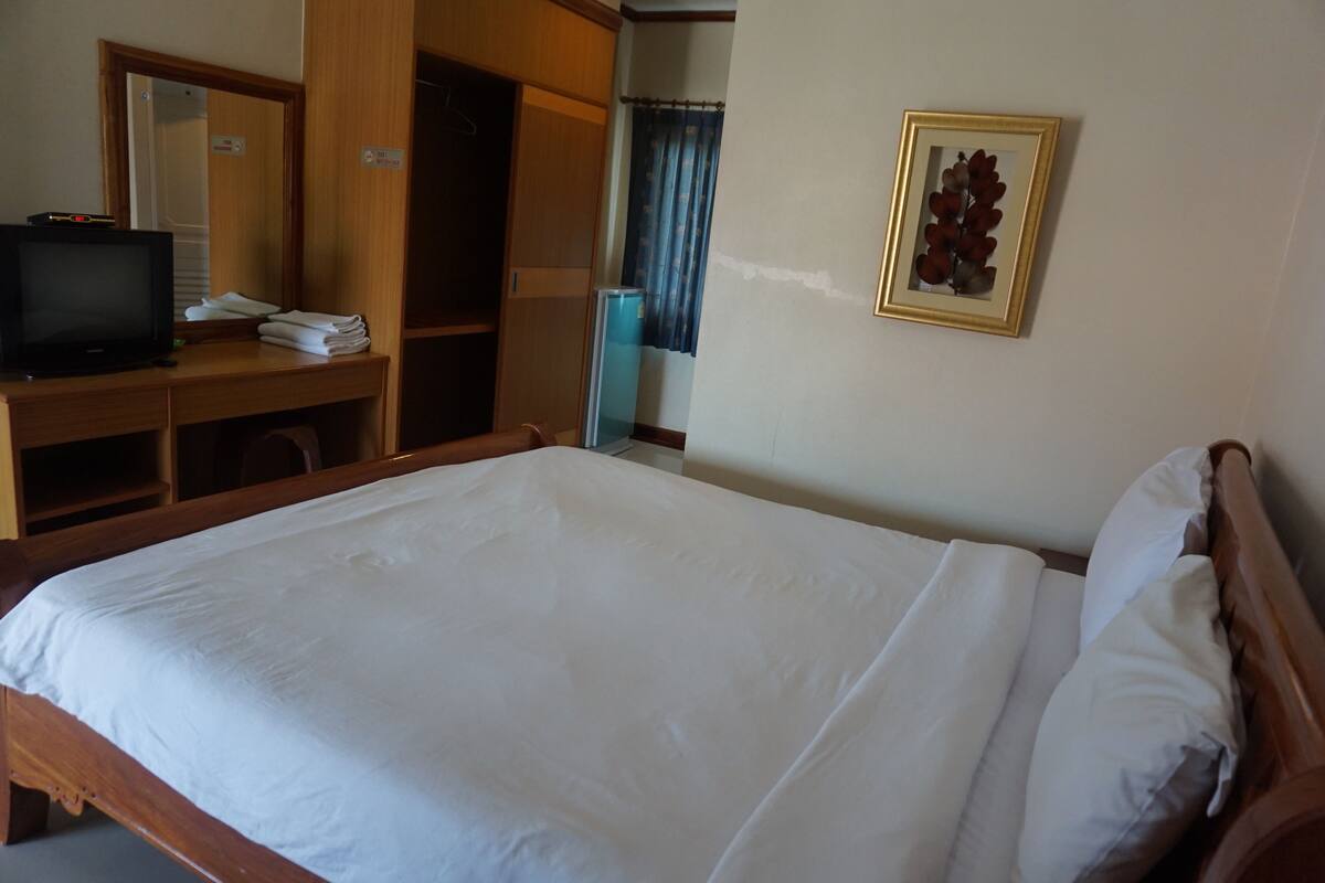 Habitación de hotel con cama, escritorio con televisor, espejo, cuadro en la pared y ventana con cortinas.