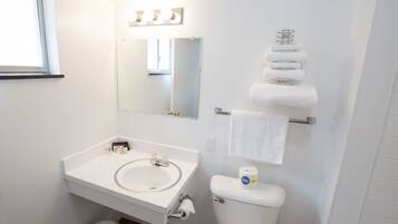 A bathroom with a white sink, mirror, and toilet. There are towels hanging on a rack and a roll of toilet paper on the wall.