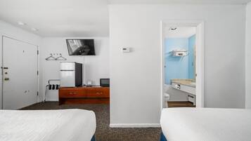 A hotel room with two beds, a desk with a computer, a TV mounted on the wall, and a bathroom visible through an open door.