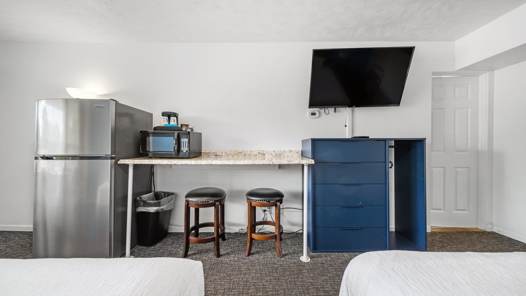 Ein kompaktes Hotelzimmer mit Küchenzeile, inklusive Kühlschrank, Mikrowelle und kleinen Barhocker.