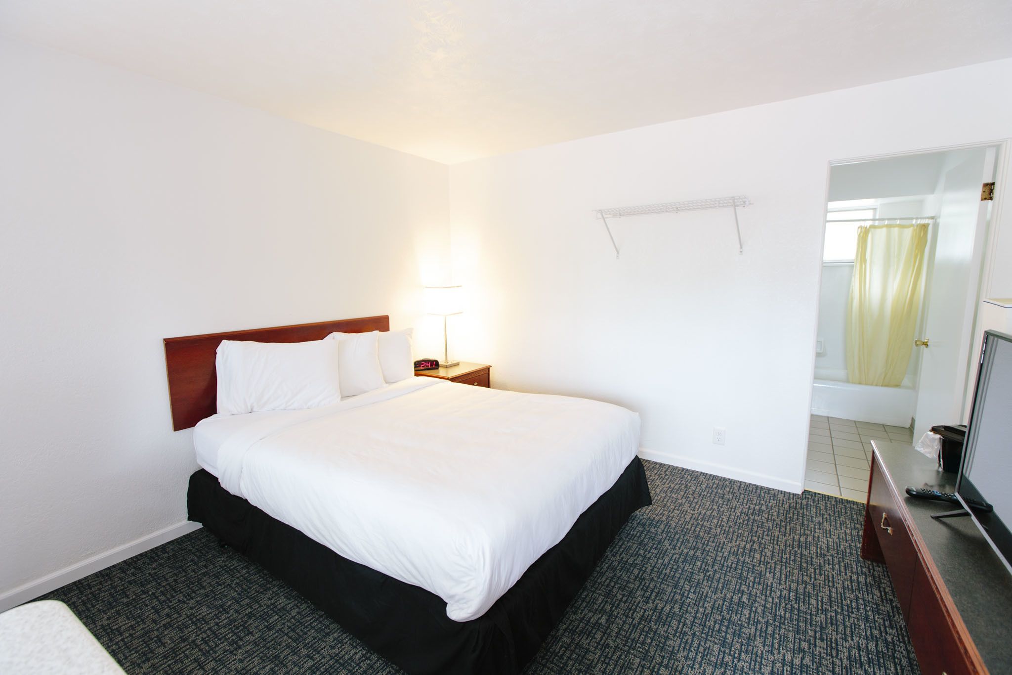 Una habitación de hotel con una cama, una mesita de noche con lámpara, un televisor y un baño visible a través de una puerta abierta.