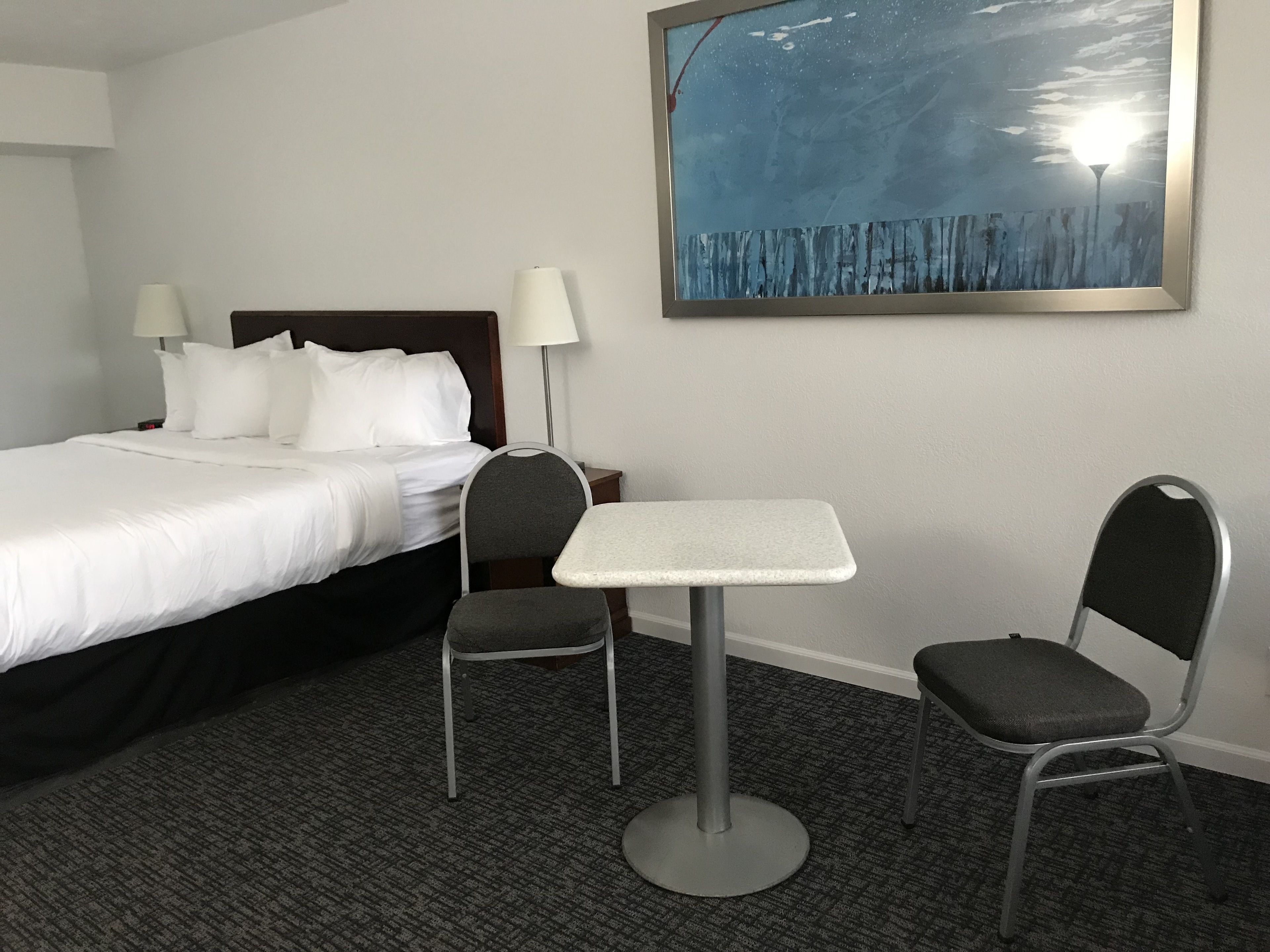 A hotel room with a bed, two chairs, a small table, and a painting on the wall.