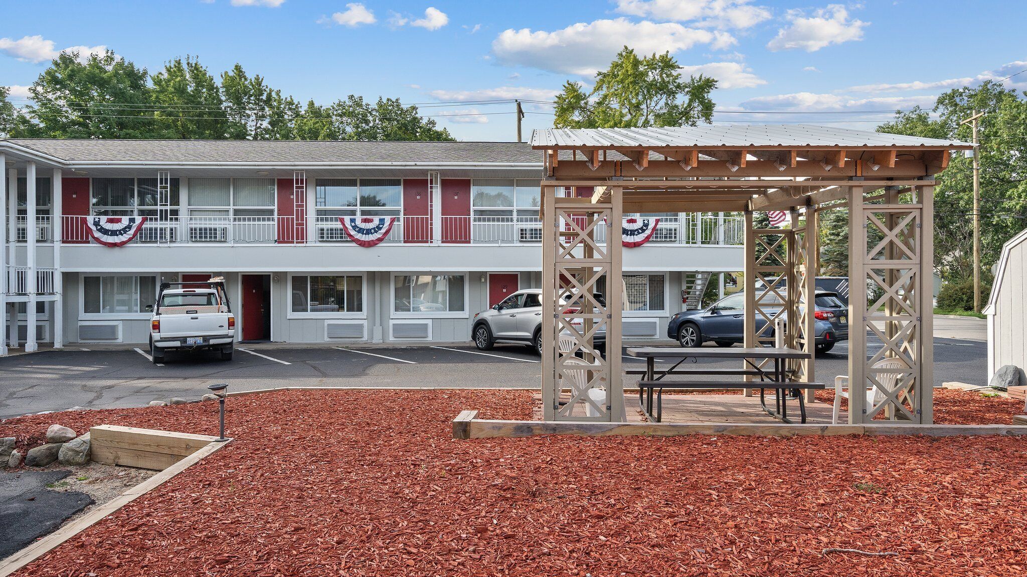 A motel with a two-story structure, a covered picnic area, and a parking lot with several cars.