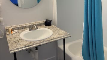 A bathroom with a white sink, a round mirror, and a blue shower curtain.