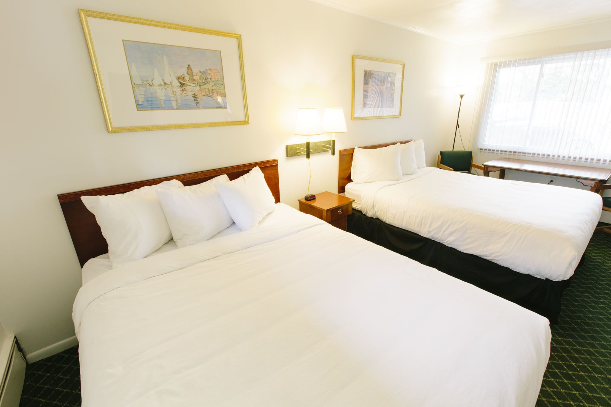 A hotel room with two beds, a desk, a chair, and framed artwork on the walls.