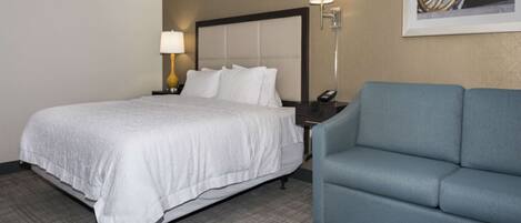 A hotel room with a bed, a blue sofa, a nightstand with a lamp, and a framed picture on the wall.
