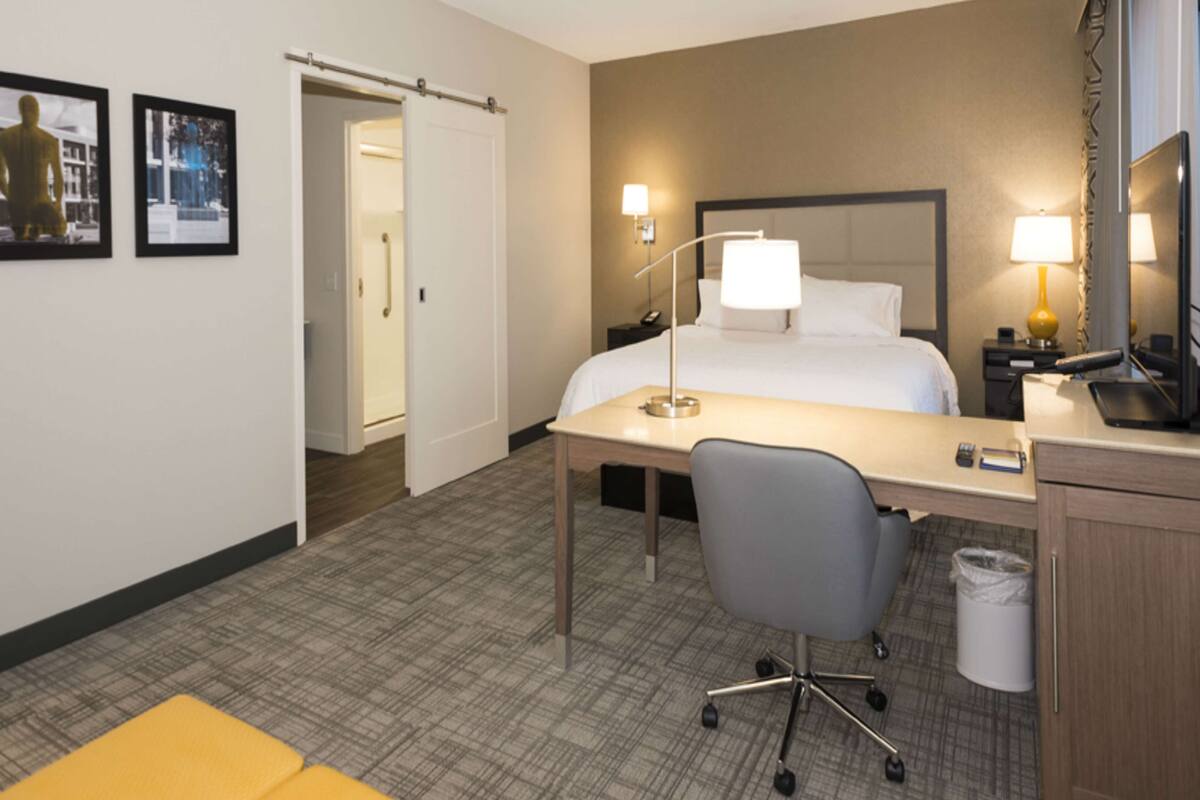 A hotel room with a bed, desk, chair, and a bathroom door.