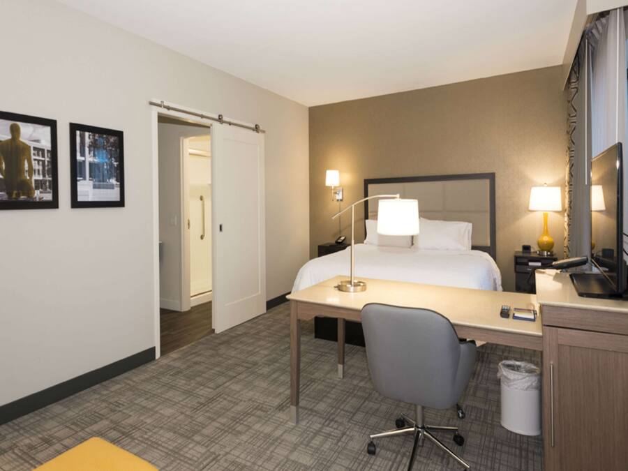 A hotel room with a bed, desk, chair, and a bathroom door.