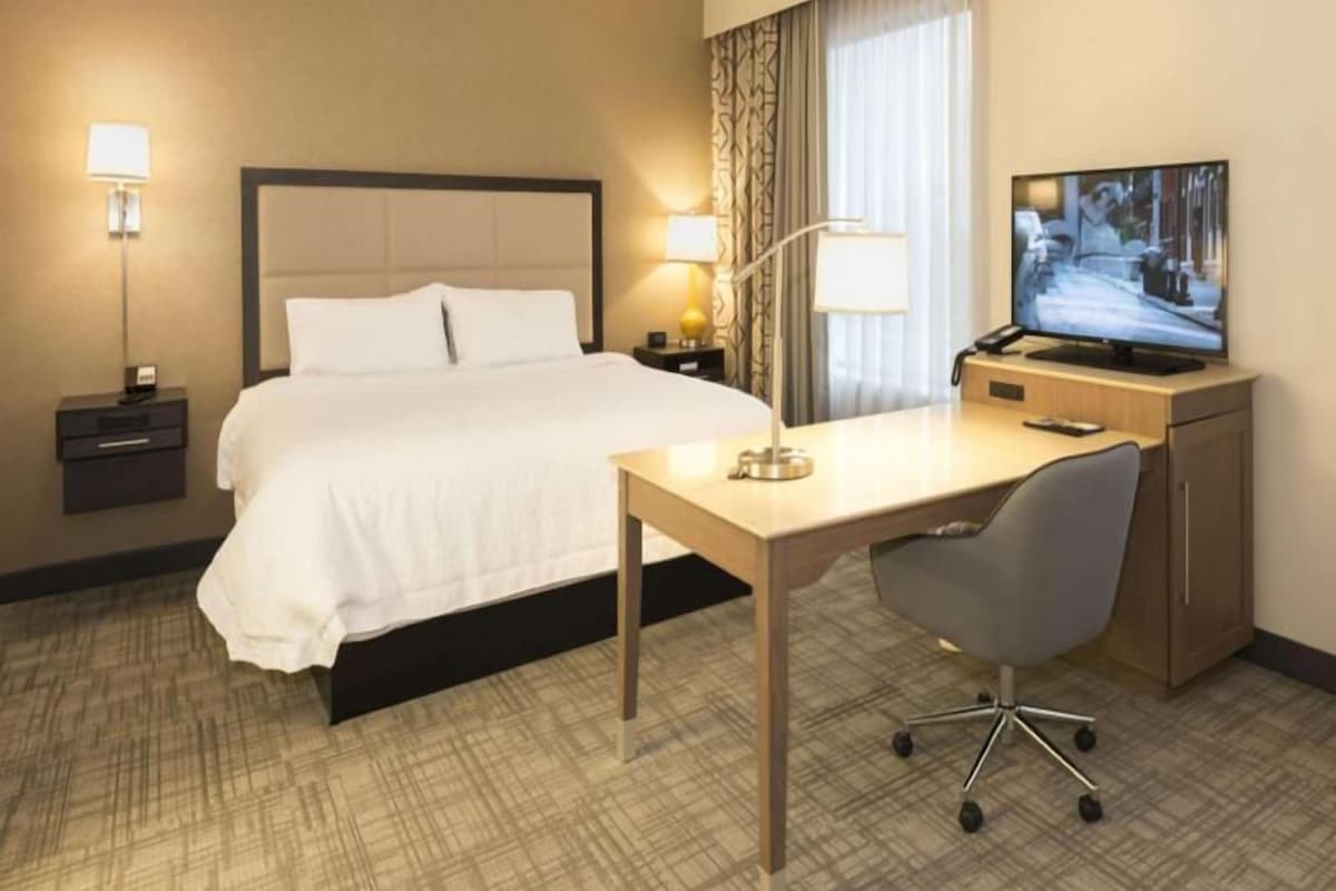Una habitación de hotel con cama, escritorio, silla, televisión y lámparas de noche.