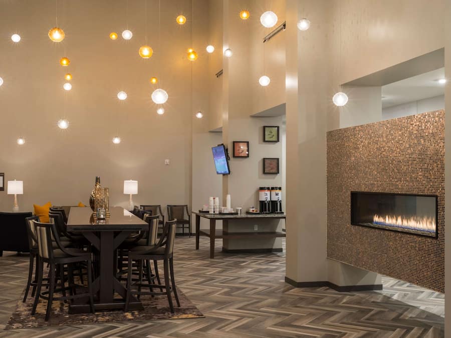 A hotel lobby with a dining area, a flat-screen TV, a coffee station, and a modern fireplace.