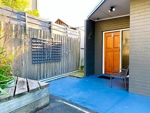 Ein Wohnhaus mit Holzzaun, einem Metalltor, einer blau gestrichenen Terrasse und einer Holztür.