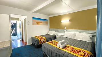 A hotel room with two beds, a blue carpet, a painting on the wall, and a bedside lamp.