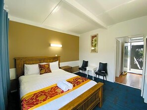 Ein Hotelzimmer mit einem großen Bett, einem Nachttisch, einem Sessel, einem kleinen Tisch und einer Tür zu einem Balkon.