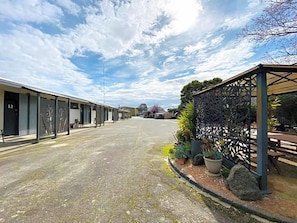 A street with a row of buildings, a covered outdoor seating area, and potted plants.