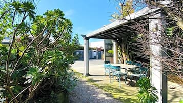 A covered outdoor seating area with tables and chairs, surrounded by greenery and a gravel path.