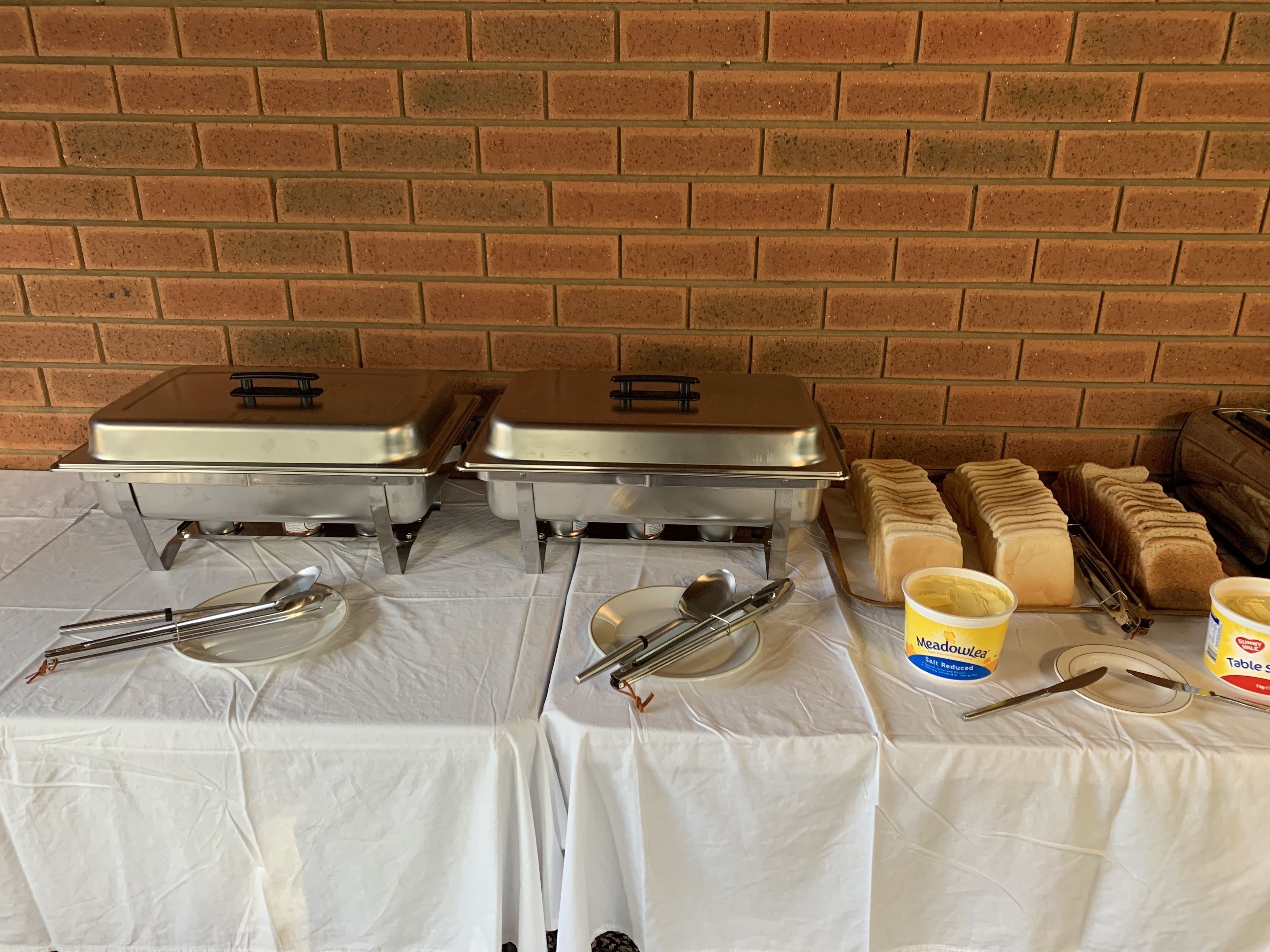 A buffet setup with two covered chafing dishes, serving utensils, and containers of butter and jam.