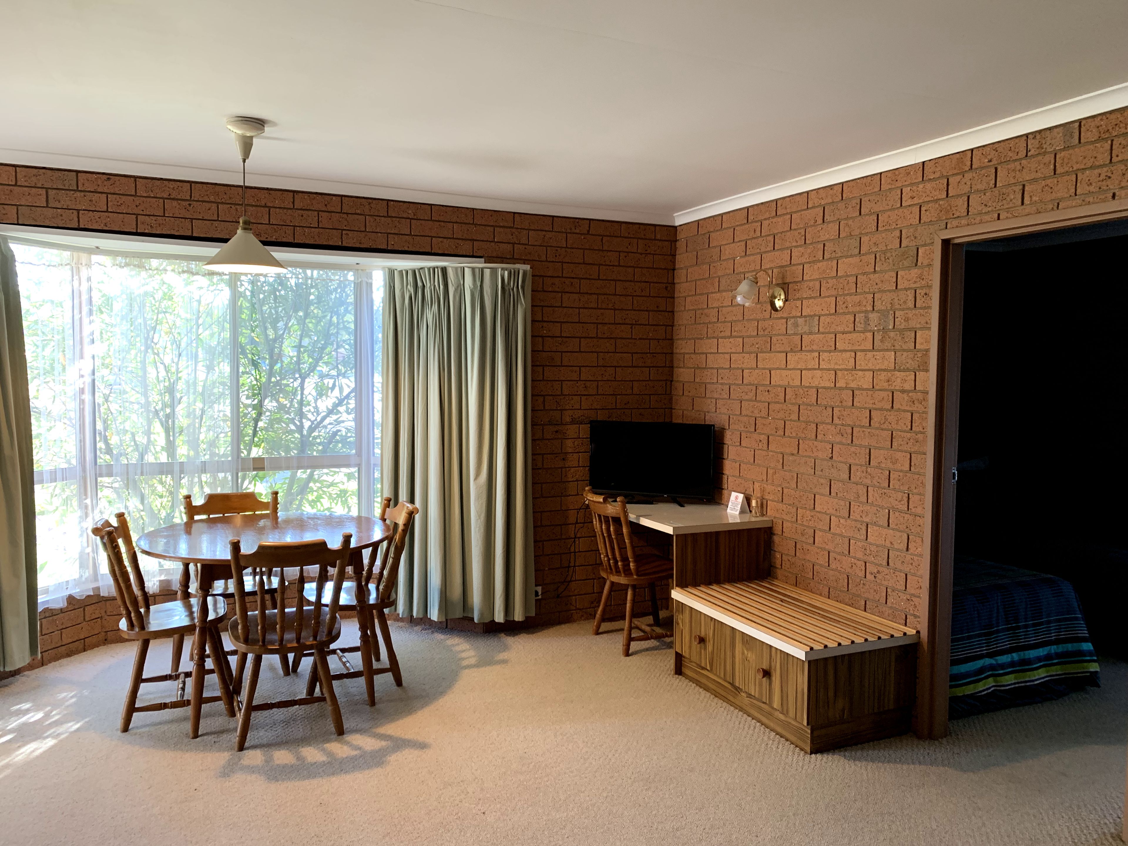 Una habitación con pared de ladrillo, una mesa de comedor con sillas, un televisor y un banco.
