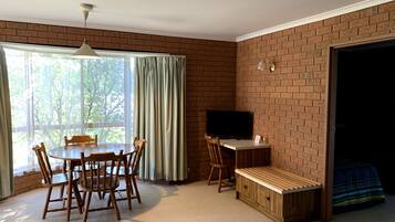 Una habitación con pared de ladrillo, una mesa de comedor con sillas, un televisor y un banco.