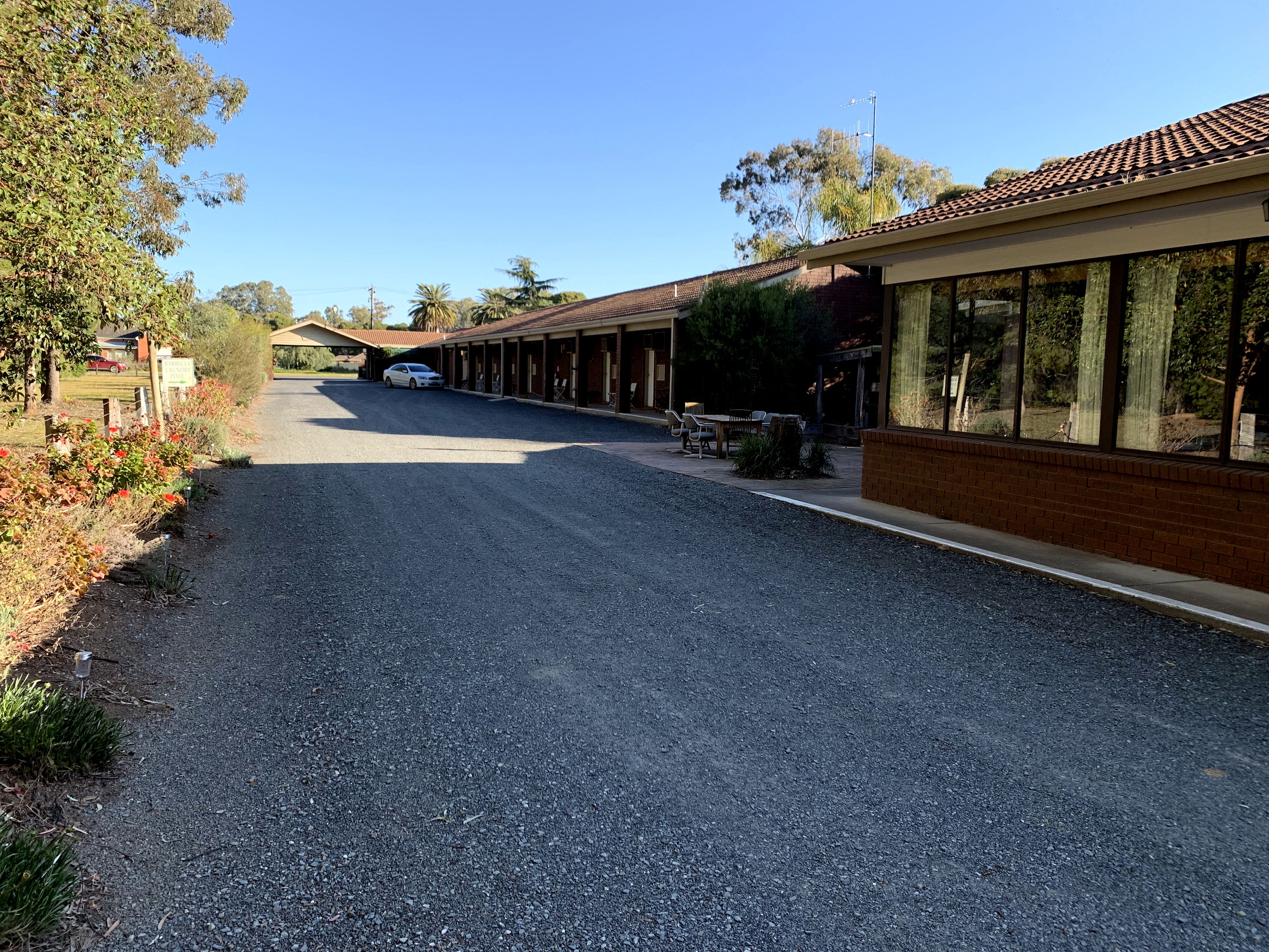 A building with a covered outdoor area, a gravel driveway, and a parked car.