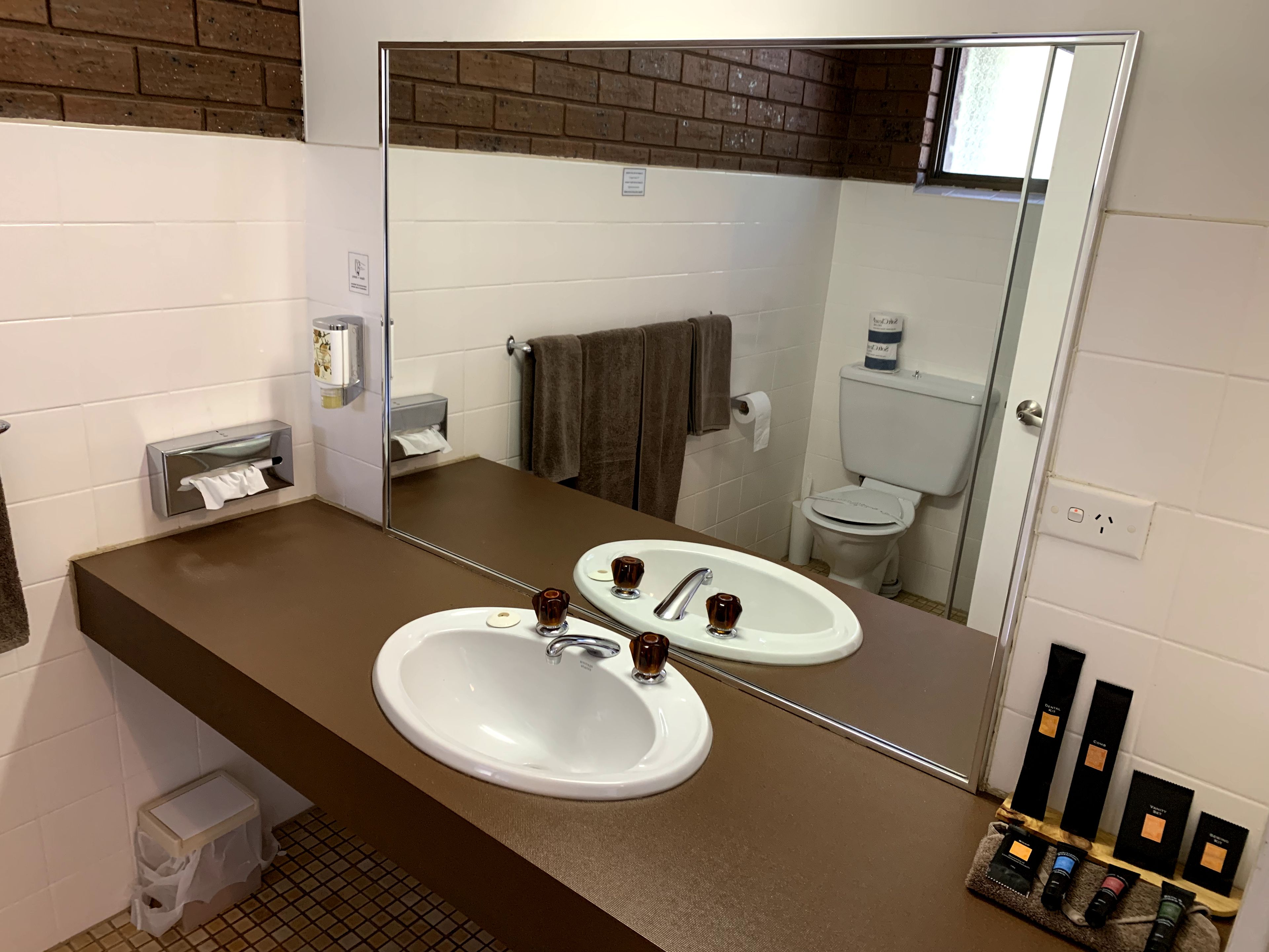 A bathroom with two sinks, a mirror, a towel rack, and a small trash bin.