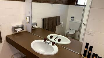 A bathroom with two sinks, a mirror, a towel rack, and a small trash bin.