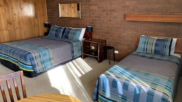 A room with two beds, a wooden table, a small desk, and a mirror on a brick wall.