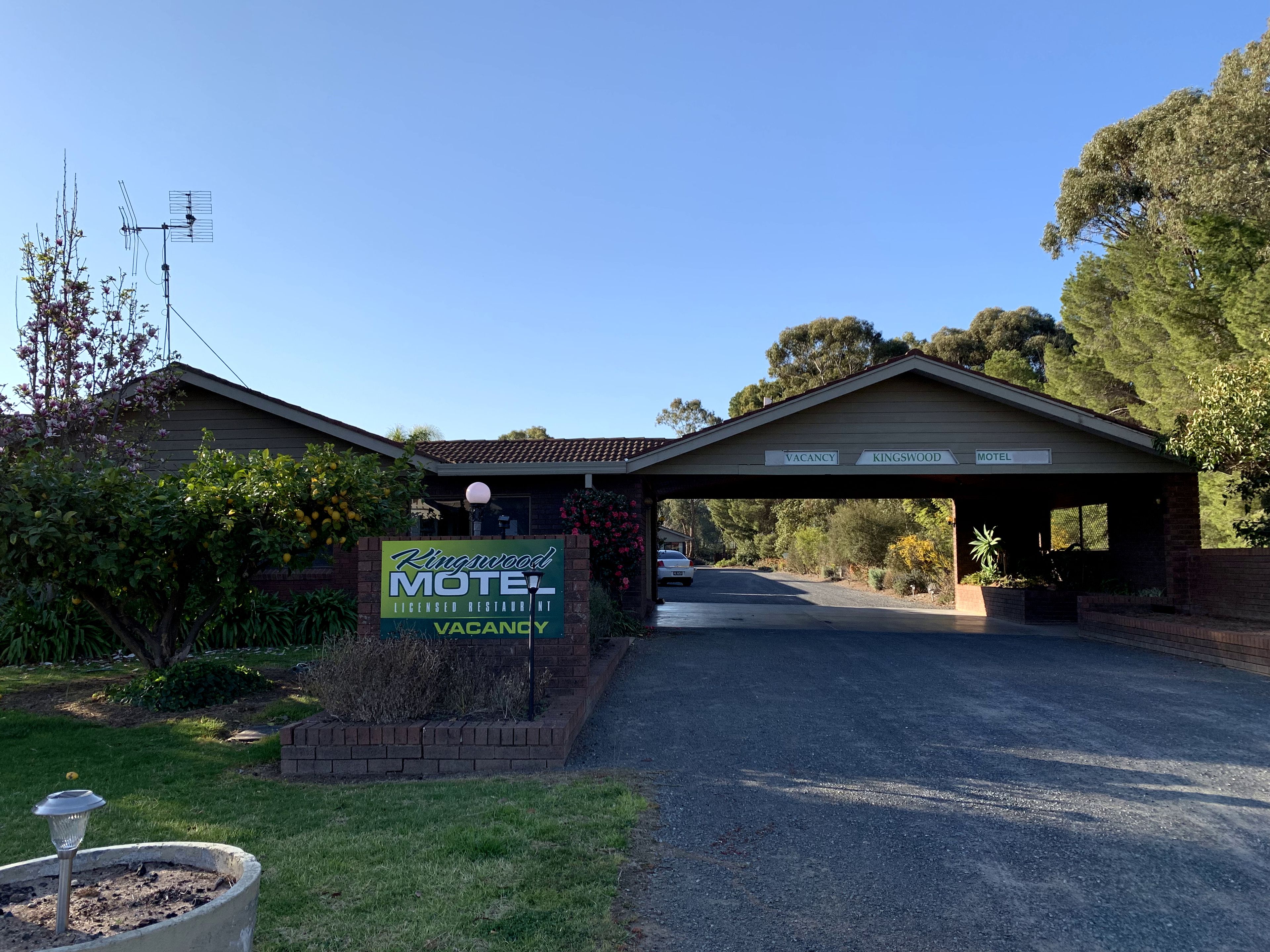 A Kingswood Motel with a 'VACANCY' sign, a covered entrance, and a driveway leading to the building.