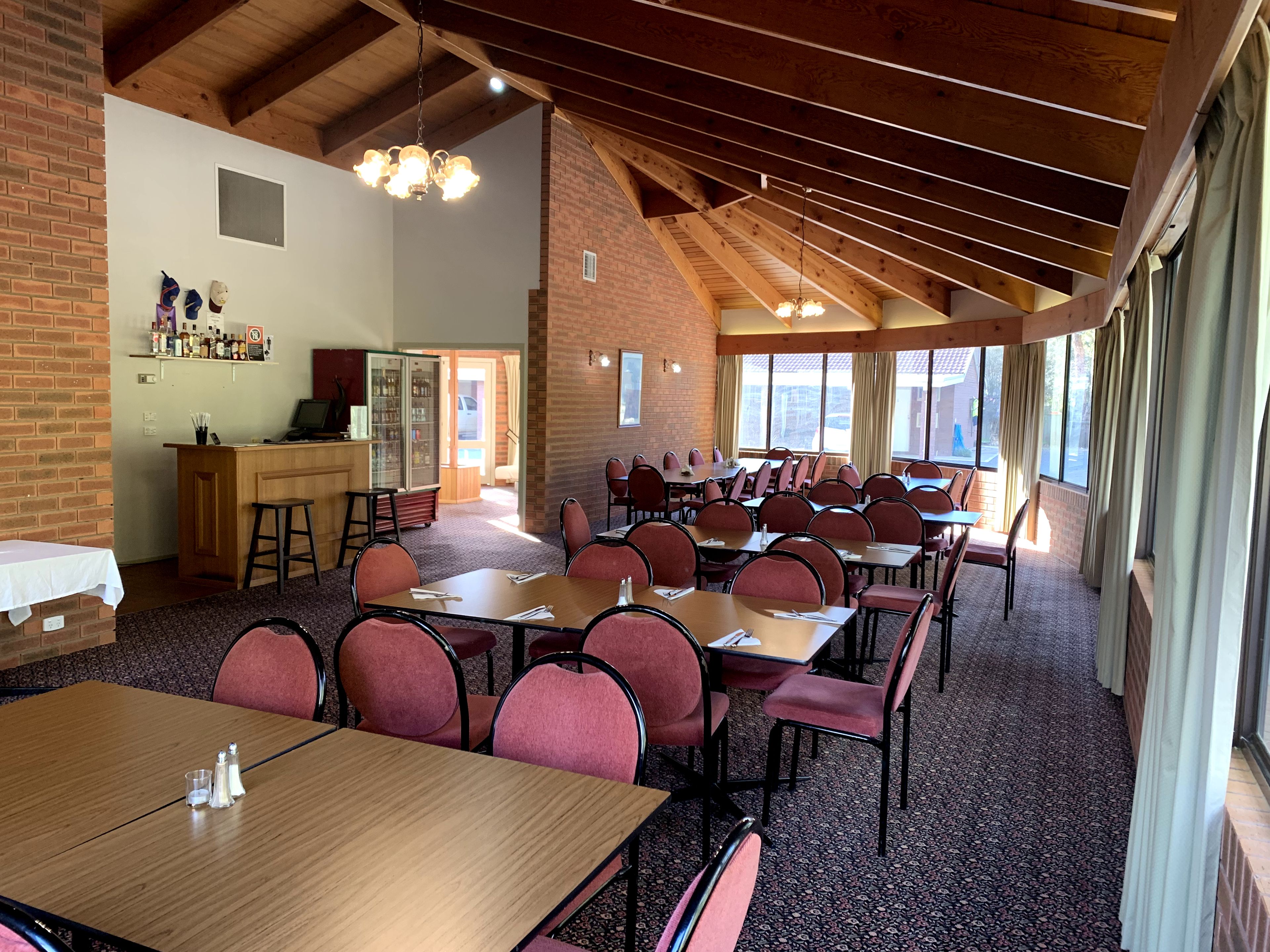 A spacious dining area with multiple tables and chairs, a kitchen area with a bar, and large windows providing natural light.