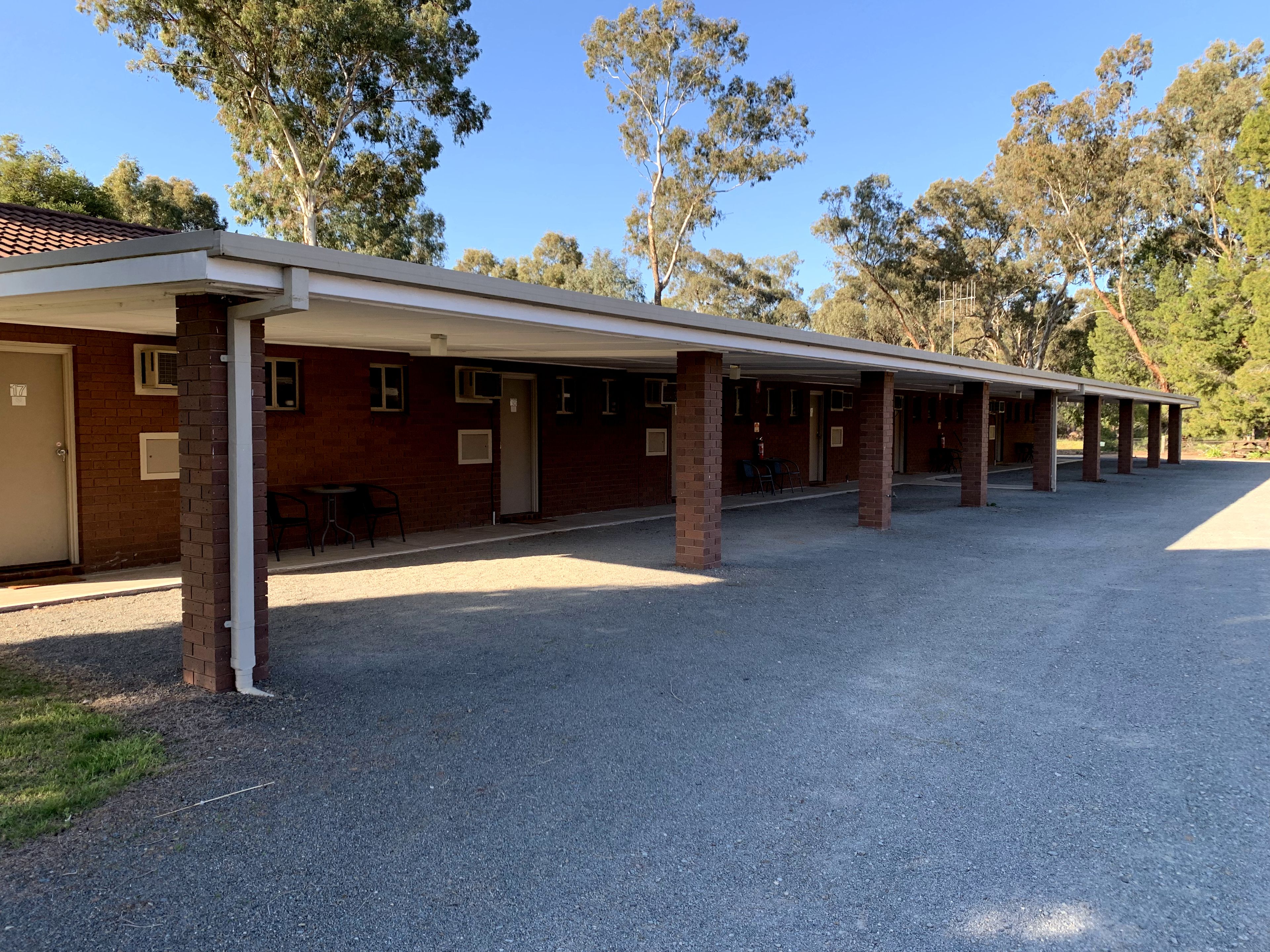 A building with a covered outdoor area, brick walls, and a gravel ground.