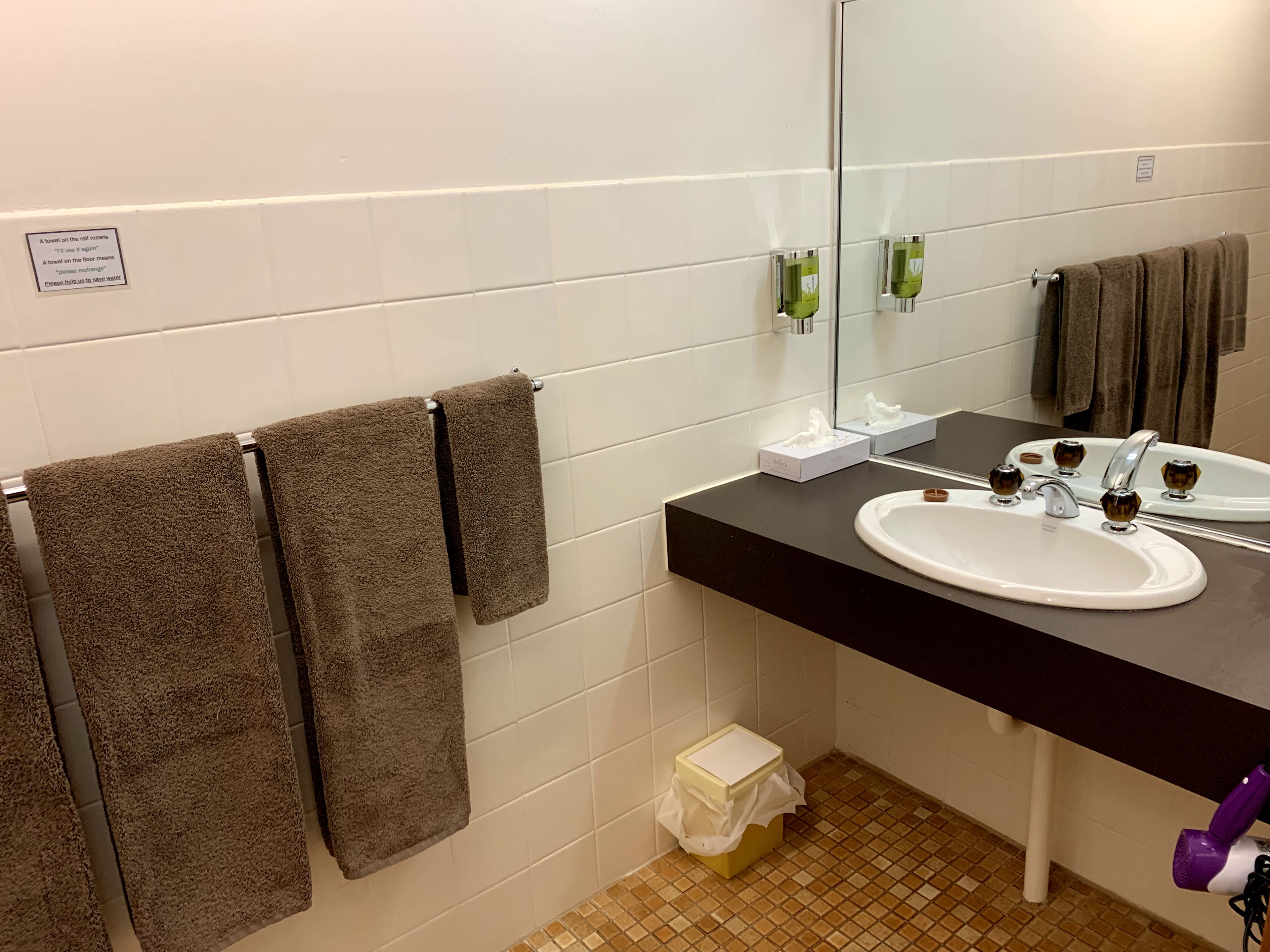 A bathroom with a black sink, two mirrors, and three towels hanging on a rack.