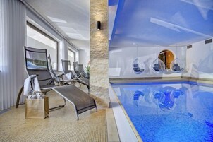 Piscina interior moderna con agua cristalina, rodeada de sillones de descanso y un pilar de piedra.
