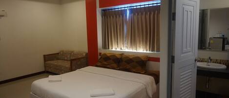 A hotel room with a bed, a chair, a window with curtains, and a bathroom with a sink and mirror.