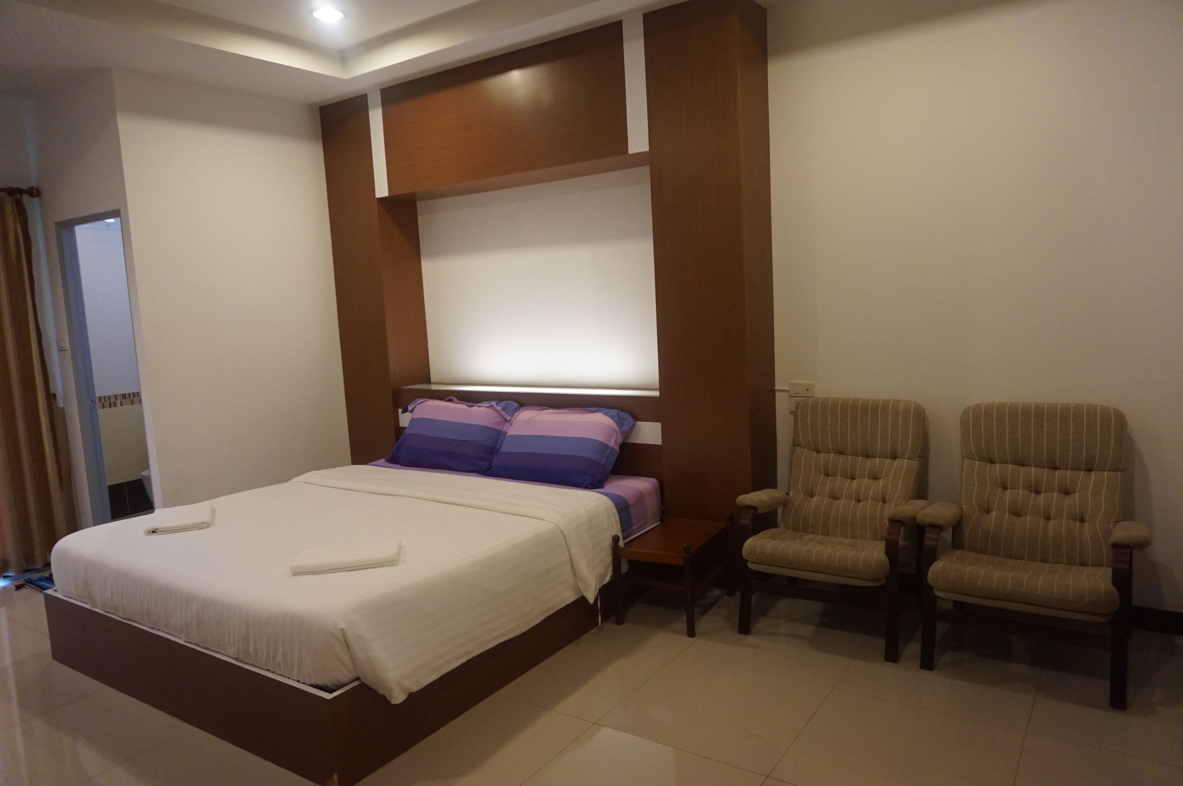 A hotel room with a large bed, a wooden headboard, a bedside table, and two upholstered chairs.