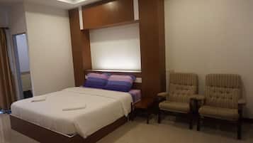 A hotel room with a large bed, a wooden headboard, a bedside table, and two upholstered chairs.